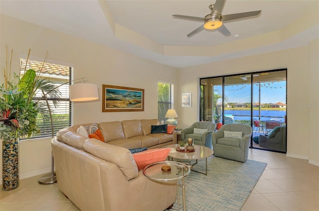 living room with ceiling fan, a raised ceiling, light tile patterned floors, and a water view