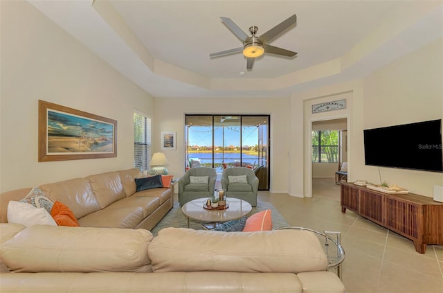 living room with a raised ceiling, ceiling fan, and light tile patterned flooring