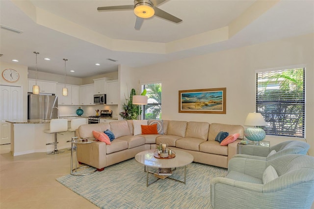 living room with ceiling fan, a raised ceiling, light tile patterned floors, and sink