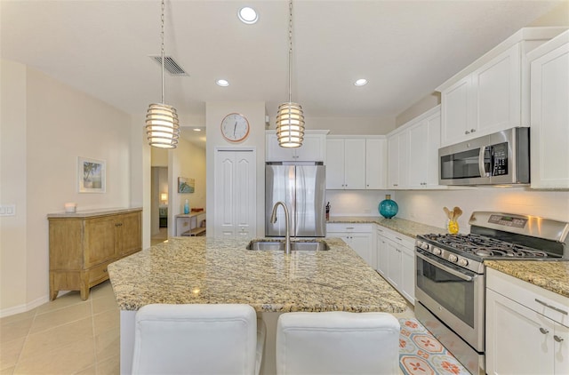 kitchen with sink, an island with sink, stainless steel appliances, and decorative light fixtures