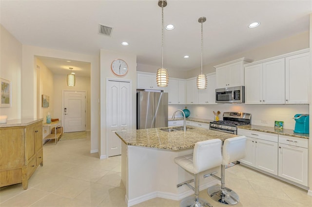 kitchen featuring stainless steel appliances, a kitchen island with sink, sink, decorative light fixtures, and white cabinetry