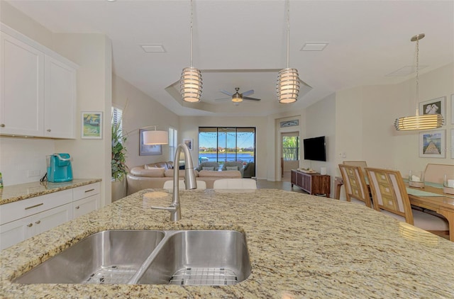 kitchen with light stone countertops, decorative light fixtures, white cabinetry, and sink