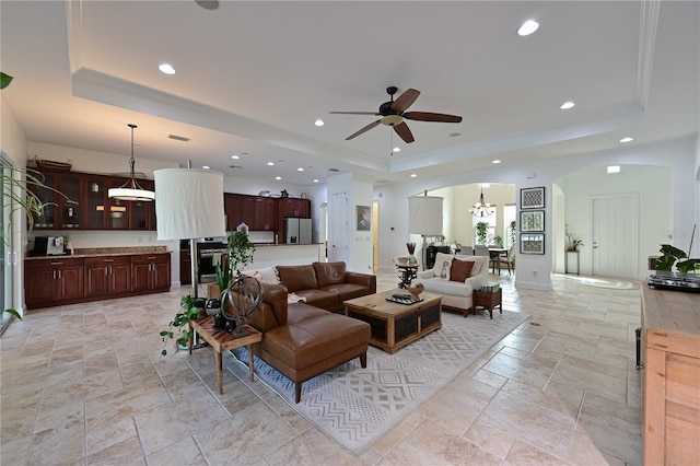 living room with ceiling fan with notable chandelier and a raised ceiling