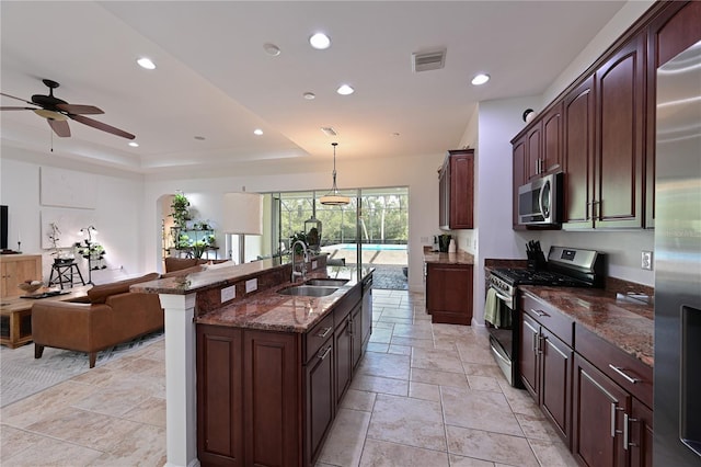 kitchen with appliances with stainless steel finishes, dark stone counters, a tray ceiling, sink, and hanging light fixtures