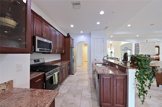 kitchen featuring a kitchen island with sink, sink, dark stone countertops, stainless steel appliances, and a chandelier