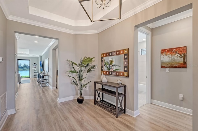 hallway featuring a raised ceiling, light hardwood / wood-style flooring, an inviting chandelier, and ornamental molding