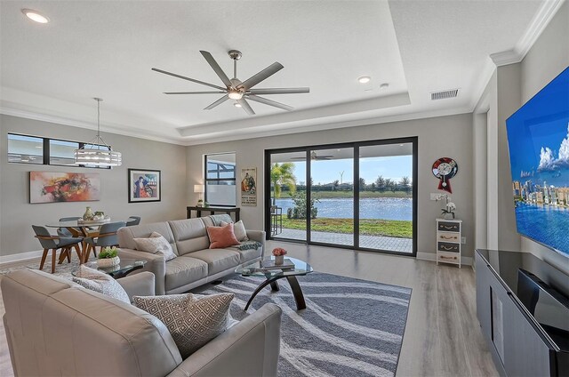 living room with ceiling fan with notable chandelier, light wood-type flooring, a tray ceiling, and ornamental molding