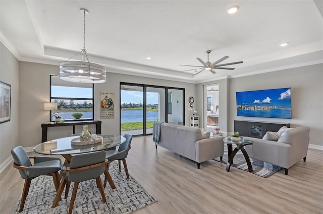 living room featuring ceiling fan with notable chandelier, a tray ceiling, crown molding, and light hardwood / wood-style floors