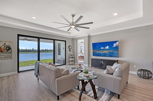 living room with ceiling fan, a raised ceiling, ornamental molding, and light hardwood / wood-style flooring