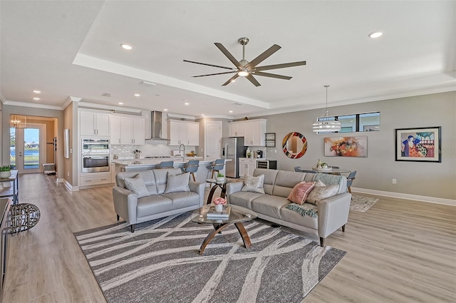 living room with ceiling fan, sink, a raised ceiling, light hardwood / wood-style flooring, and ornamental molding