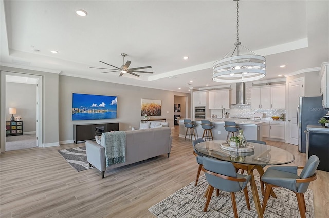 dining area with ceiling fan with notable chandelier, light hardwood / wood-style floors, a raised ceiling, and sink