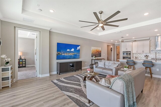 living room featuring ceiling fan, a raised ceiling, light wood-type flooring, and ornamental molding