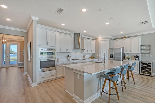 kitchen featuring sink, wall chimney exhaust hood, stainless steel appliances, beverage cooler, and a kitchen island with sink