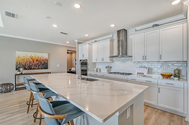 kitchen with white cabinetry, a kitchen island with sink, wall chimney exhaust hood, and a breakfast bar area