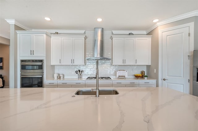 kitchen featuring white cabinets, appliances with stainless steel finishes, light stone counters, and wall chimney exhaust hood