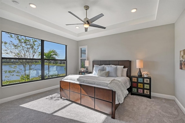 carpeted bedroom featuring a water view, a raised ceiling, and ceiling fan