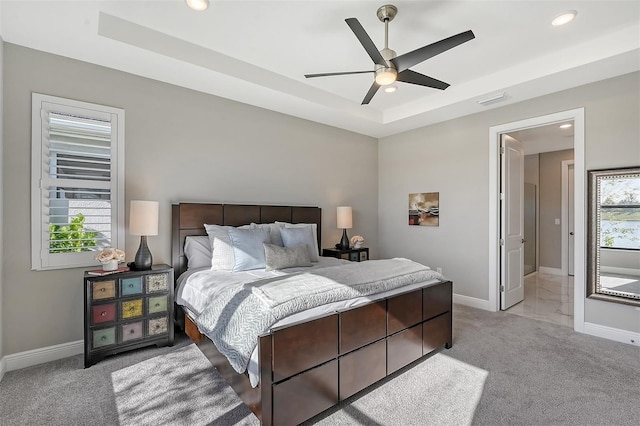 carpeted bedroom with multiple windows, a raised ceiling, and ceiling fan