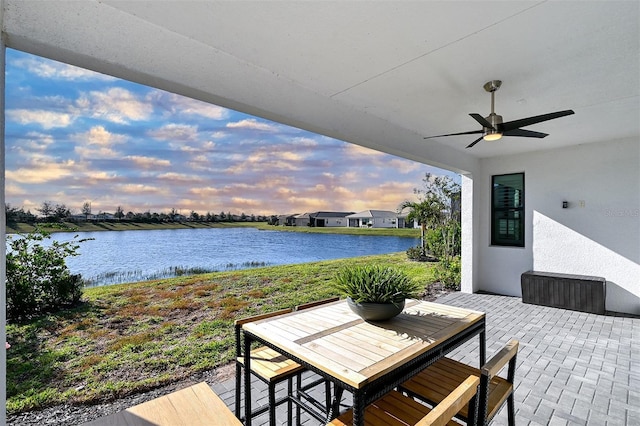 patio terrace at dusk featuring ceiling fan and a water view