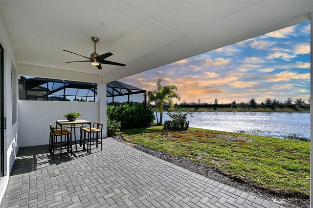 patio terrace at dusk featuring a lanai, ceiling fan, and a water view