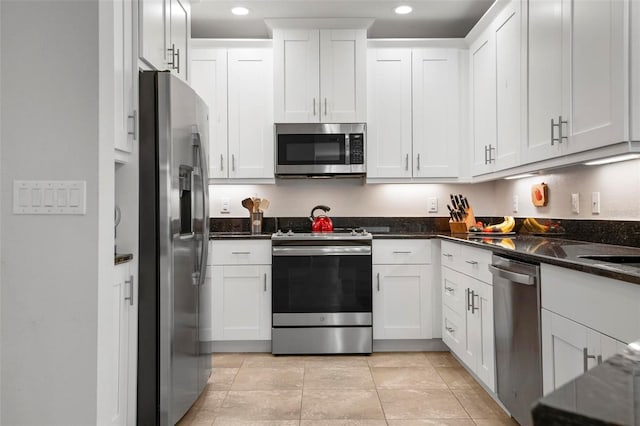 kitchen featuring white cabinets, light tile patterned floors, appliances with stainless steel finishes, and dark stone counters