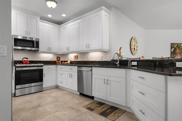 kitchen with appliances with stainless steel finishes, white cabinetry, dark stone counters, and sink