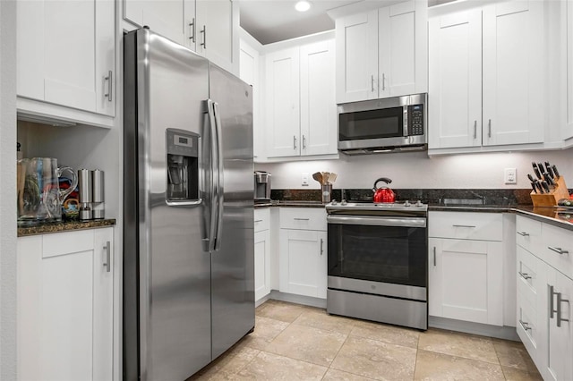 kitchen with white cabinetry, stainless steel appliances, and dark stone counters