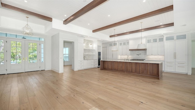 kitchen with light wood-type flooring, tasteful backsplash, a spacious island, pendant lighting, and white cabinets