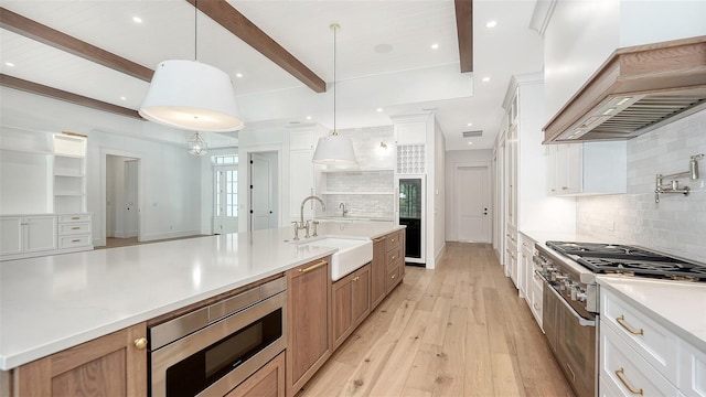 kitchen with pendant lighting, sink, beamed ceiling, white cabinetry, and stainless steel appliances