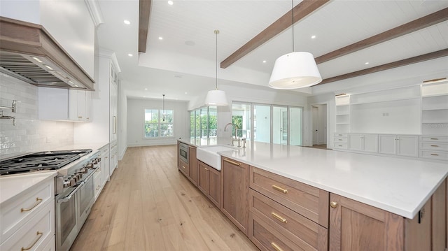 kitchen featuring custom range hood, sink, double oven range, white cabinets, and hanging light fixtures