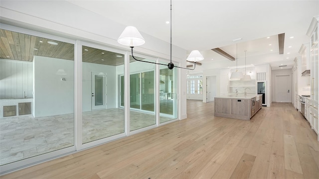 interior space featuring pendant lighting, sink, an island with sink, light hardwood / wood-style floors, and white cabinetry