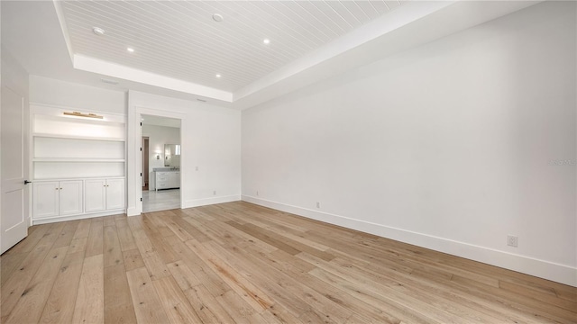 unfurnished living room featuring built in features, a tray ceiling, and light hardwood / wood-style flooring