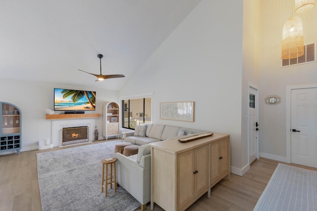 living room with ceiling fan, built in features, high vaulted ceiling, and light hardwood / wood-style flooring