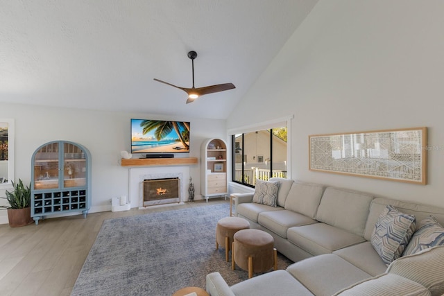 living room with ceiling fan, built in features, a textured ceiling, vaulted ceiling, and light wood-type flooring