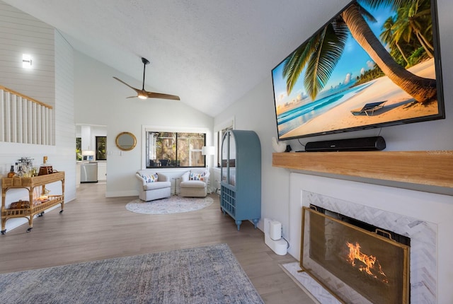 living room featuring a textured ceiling, ceiling fan, wood-type flooring, high vaulted ceiling, and a premium fireplace