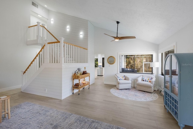 living room featuring a textured ceiling, light hardwood / wood-style floors, high vaulted ceiling, and ceiling fan