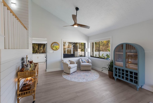 living room featuring a textured ceiling, ceiling fan, light hardwood / wood-style flooring, and vaulted ceiling