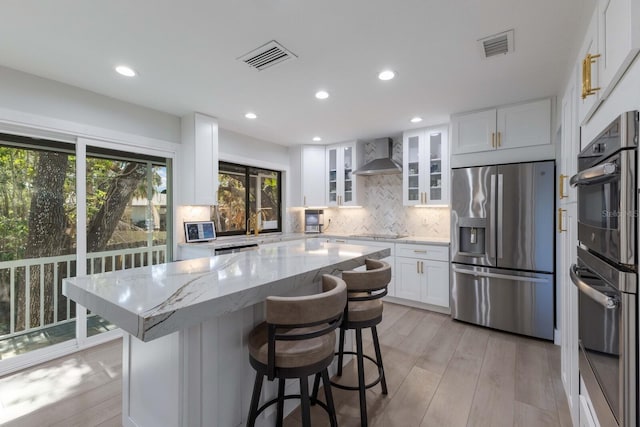 kitchen featuring decorative backsplash, appliances with stainless steel finishes, wall chimney range hood, white cabinets, and a center island