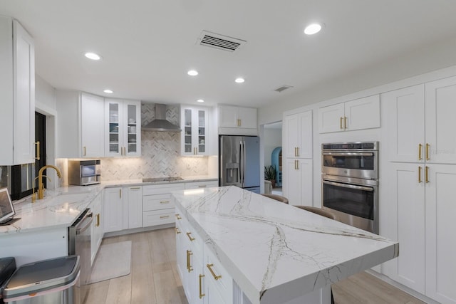 kitchen featuring white cabinetry, a center island, wall chimney range hood, tasteful backsplash, and appliances with stainless steel finishes