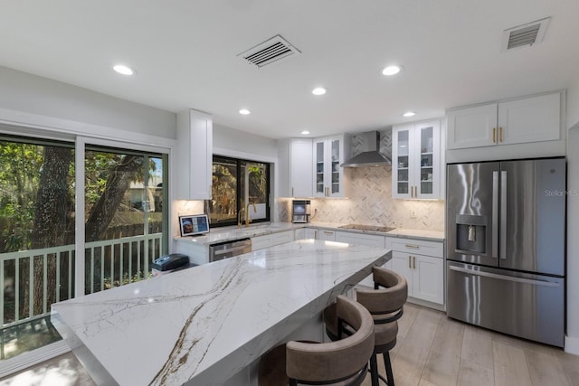 kitchen with tasteful backsplash, light stone counters, wall chimney exhaust hood, stainless steel appliances, and white cabinets