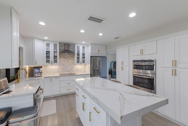 kitchen with stainless steel appliances, wall chimney range hood, a kitchen island, tasteful backsplash, and white cabinets