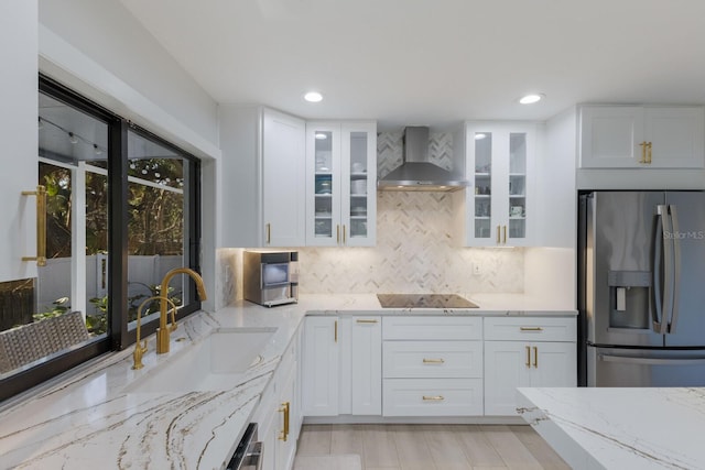 kitchen featuring stainless steel refrigerator with ice dispenser, sink, white cabinetry, and wall chimney range hood