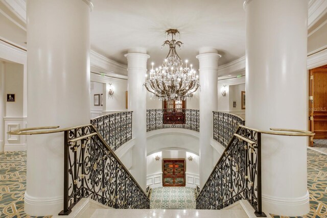 stairs featuring a notable chandelier, ornamental molding, and a high ceiling