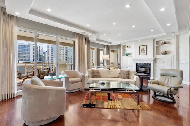 living room featuring a high end fireplace, built in shelves, dark hardwood / wood-style floors, and a tray ceiling