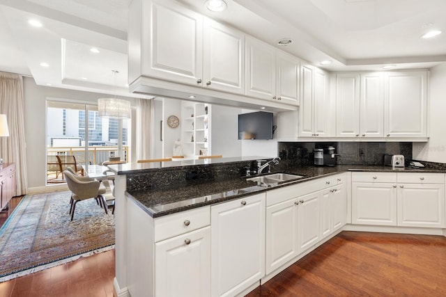 kitchen with white cabinetry, kitchen peninsula, sink, and a tray ceiling