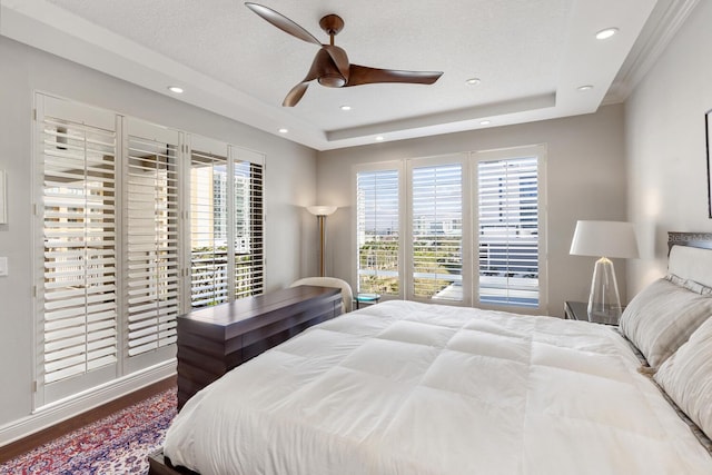 bedroom featuring hardwood / wood-style floors, a textured ceiling, a raised ceiling, and ceiling fan