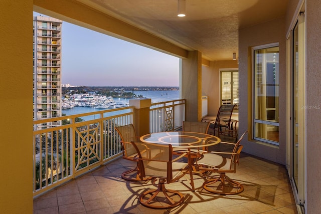 balcony at dusk featuring a water view