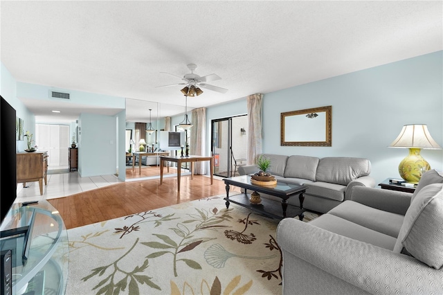 living room with ceiling fan, light hardwood / wood-style floors, and a textured ceiling