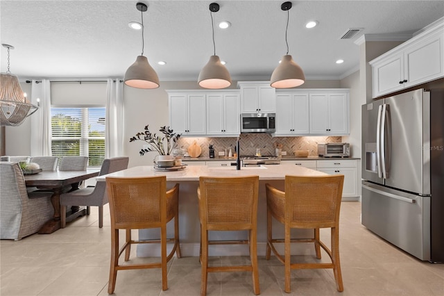 kitchen with white cabinets, appliances with stainless steel finishes, pendant lighting, and an island with sink