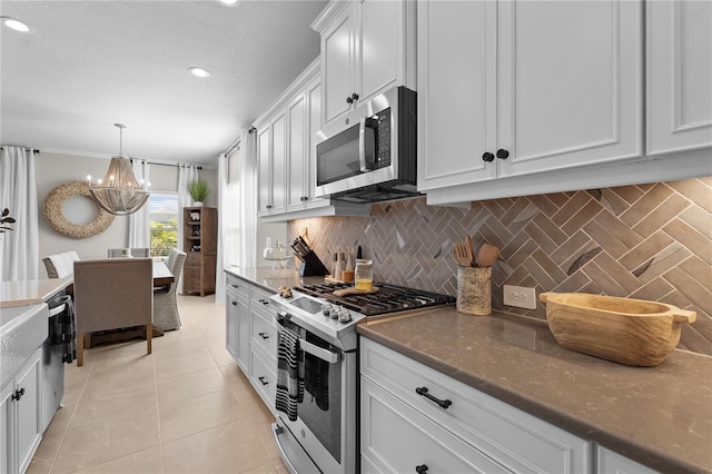 kitchen with appliances with stainless steel finishes, tasteful backsplash, light tile patterned floors, an inviting chandelier, and white cabinets