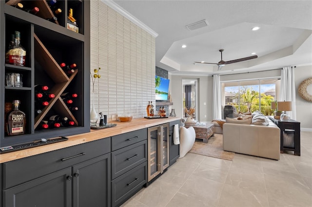 interior space featuring bar, ceiling fan, wine cooler, and a tray ceiling